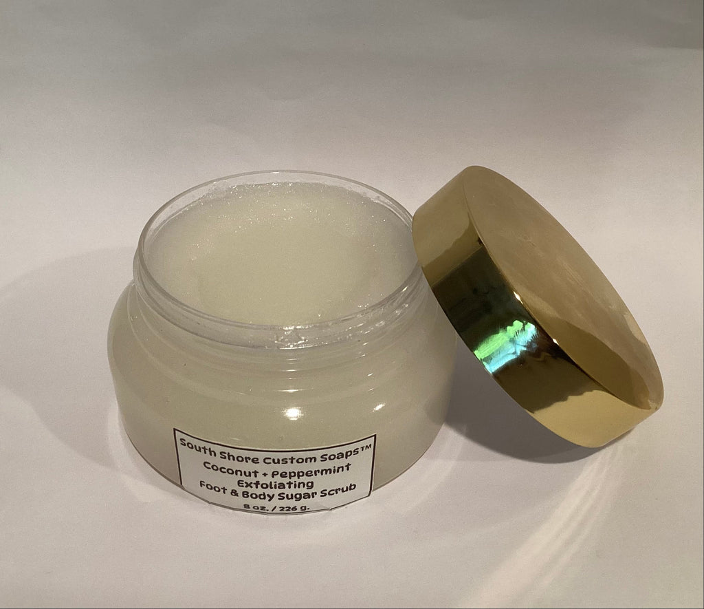 A jar of foot and body sugar scrub with its metallic gold lid leaning against it on a white background. The label reads 'South Shore Custom Soaks Coconut + Peppermint Exfoliating Foot & Body Sugar Scrub'.